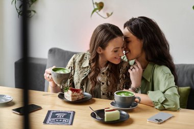 Neşeli bir lezbiyen çift, tatlı bir anı paylaşırken aynı anda hem Matcha içkilerinin hem de tatlılarının tadını çıkarıyor..