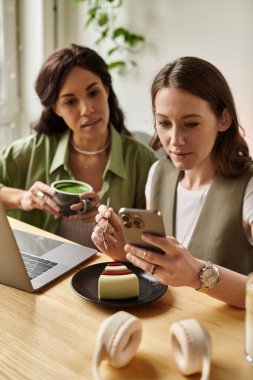İki kadın bir kafede birlikte olmaktan hoşlanır, tatlılarını paylaşırlar ve birlikte telefona bakarlar..