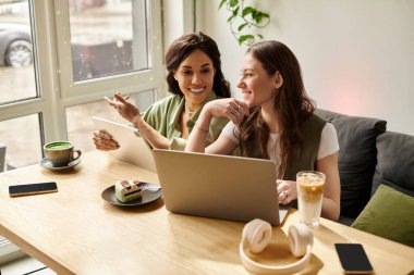 Bir kafede dizüstü bilgisayarla çalışırken iki kadın kahve içerken kahkaha ve fikir paylaşıyor..