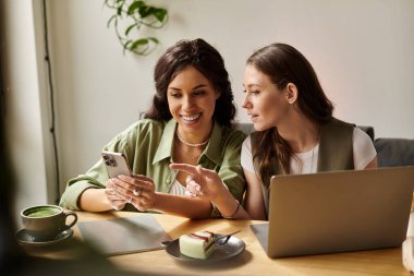İki kadın, rahat bir kafede telefonlarını kontrol ederken birbirlerine eşlik etmekten mutlu olurlar..
