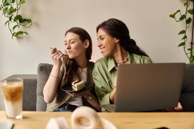 İki kadın bir kafede dizüstü bilgisayarla çalışırken tatlıdan ve kahkahadan zevk alır..