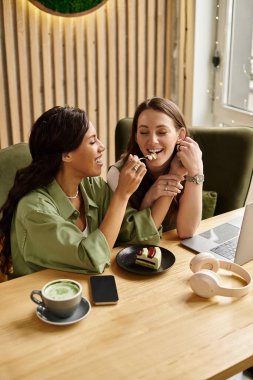 İki kadın tatlı bir tatlıyı paylaşırken birlikte bir kafe ortamında vakit geçiriyorlar..