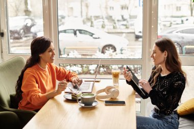 Sıcak bir atmosferi olan rahat bir kafede iki kadın mutlu bir şekilde sohbet ediyor..