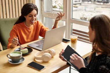 İki kadın, sıcak bir kafede içki ve tatlı içerken aynı kahkaha ve bağlantıyı paylaşıyor..