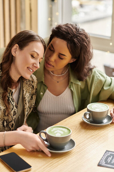 Two women enjoy each others company over cups of green tea in a warm and inviting cafe.