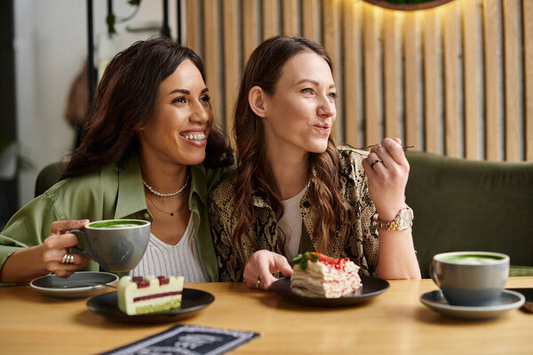 Two women share a joyful moment at a charming cafe, savoring pastries and delightful drinks.