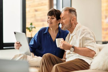 Neşeli bir çift birlikte oturup tablet üzerinde kahkaha ve heyecan paylaşıyor..