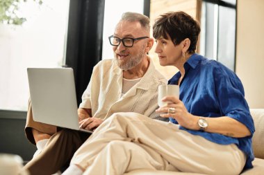 Neşeli bir çift, rahat evlerinde dizüstü bilgisayar kullanırken birlikte içmeyi ve gülmeyi sever..