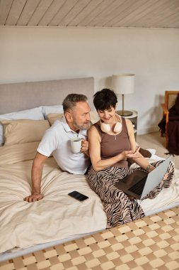 Orta yaşlı çift evlerinde dizüstü bilgisayarlarında birlikte çalışarak keyifli bir anı paylaşıyorlar..