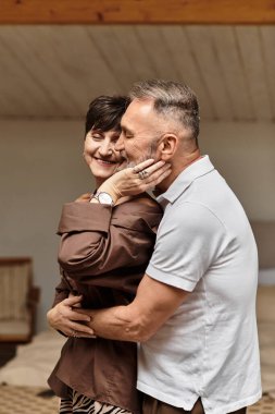 Mutlu orta yaşlı bir çift evde sevgi ve neşe saçan şefkatli bir kucaklaşmayı paylaşıyor..
