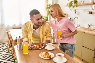 Bir çift, evlerinin mutfağında kruvasan ve içeceklerle keyifli bir kahvaltı yapar..