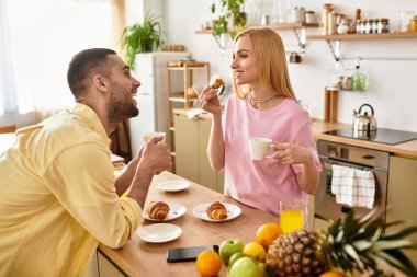 Erkek ve kadın, evde kahkaha ve sıcak kahveyi paylaşırken keyifli bir kahvaltı yaparlar..