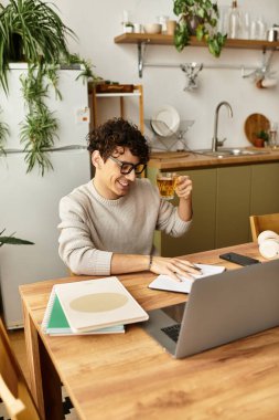 Yakışıklı genç adam masasında çalışırken gülümsüyor, rahat bir ortamda içkisini yudumluyor..
