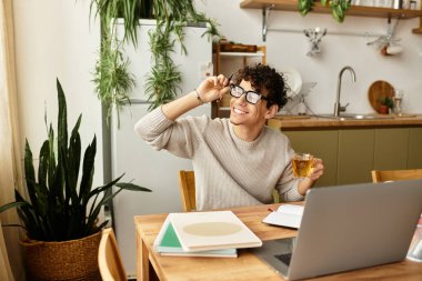 Şık gözlüklü neşeli genç adam sıcak bir mutfakta çay içerken rahatlıyor..