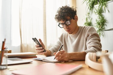 Yakışıklı genç adam evde akıllı telefonunu kullanırken dikkatle not yazmaya odaklanıyor..