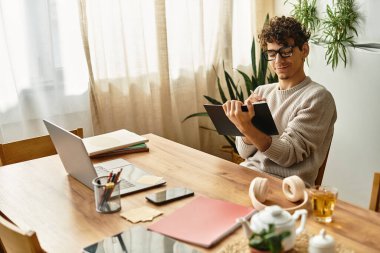 Adam ahşap bir masada oturuyor, defterine odaklanmış, bitkiler ve sıcak güneş ışığı ile çevrili..