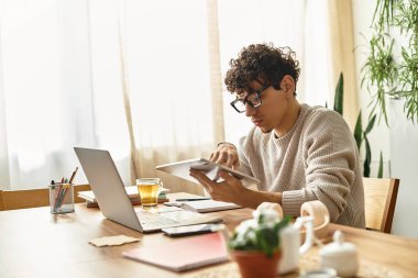 Rahat bir süveter giyen genç yakışıklı, parlak bir çalışma alanında dijital tabletle meşgul oluyor..