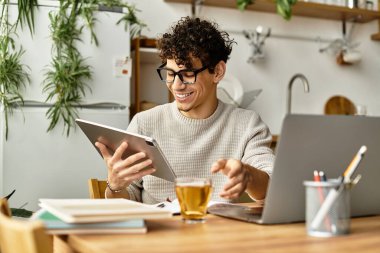 Kıvırcık saçlı, gülümseyen genç bir adam bitkilerle çevrili, modaya uygun bir kafede tabletle meşgul oluyor..