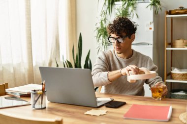 Rahat süveter giyen yakışıklı adam laptopunda dikkatlice çalışırken çay hazırlıyor..