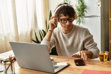 Kıvırcık saçlı ve gözlüklü yakışıklı adam yeşil ve ışıkla çevrili telefonuna odaklanıyor..