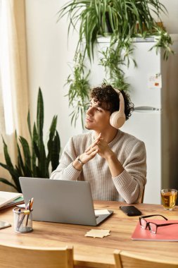 Şık kulaklıklı genç bir adam ahşap bir masada, çalışırken derin düşüncelere dalmış oturuyor..