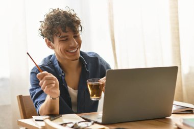 Şık bir genç adam elinde bir içki tutarken ve bilgisayarının başında rahat bir şekilde çalışırken ışıl ışıl gülümser..