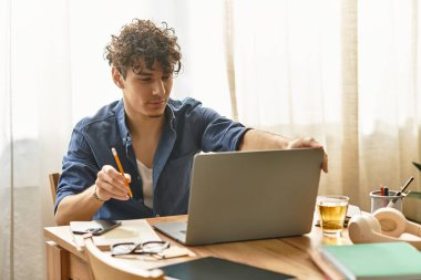 Yakışıklı genç adam, içi notlarla dolu ahşap bir masada otururken dikkatle dizüstü bilgisayarda çalışıyor..