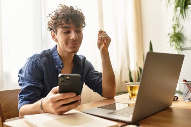 Yakışıklı adam akıllı telefonuyla iletişim kuruyor, evde sıcak bir içkinin tadını çıkarırken gülümsüyor..