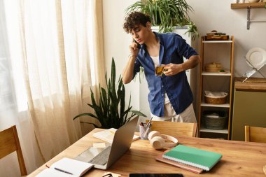 Yakışıklı genç adam telefonda konuşuyor ve rahat, modern bir evde bir içki yudumluyor..