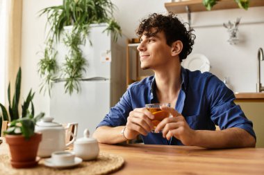 Genç adam, canlı bitkilerle çevriliyken, parlak bir mutfakta çayın tadını çıkarıyor..