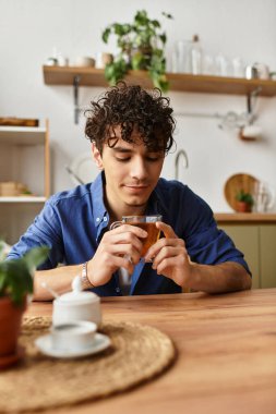 Yakışıklı genç bir adam ahşap bir masada oturuyor, yeşil alanla çevrili iken sıcak bir içkinin tadını çıkarıyor..