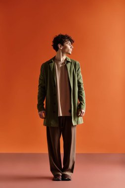 Genç, yakışıklı bir adam parlak turuncu bir arka plana karşı şık kıyafetini sergiliyor..