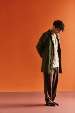 Şık giyinmiş genç bir adam canlı renkler ve yumuşak ışıkların arasında düşünceli bir şekilde duruyor..