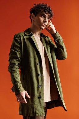 Kendine güveni olan, kıvırcık saçlı şık bir zeytin palto giyen ve rahat giyinen şık bir genç.