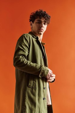 Yakışıklı bir genç adam, turuncu bir duvarın önünde dikilirken şık bir moda sergiliyor..