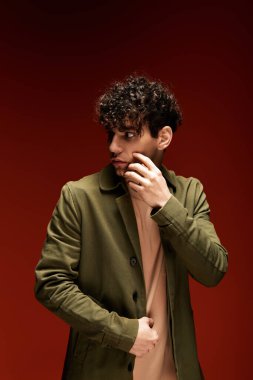 Kıvırcık saçlı yakışıklı bir adam düşünceli bir poz verirken şık bir kıyafet sergiliyor..