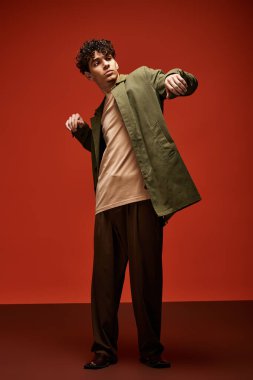 Şık bir genç adam, modaya uygun kıyafetiyle cesur bir kırmızı arka plana karşı güvenle poz veriyor..