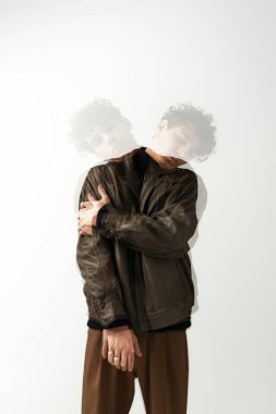 Şık kahverengi deri ceketli genç adam çapraz kollu sanatsal hareket gösteriyor..