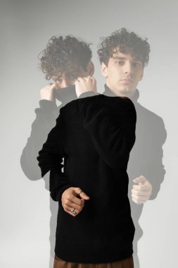 Kıvırcık saçlı yakışıklı bir adam, minimalist bir arkaplana karşı şık bir kıyafet sunar..