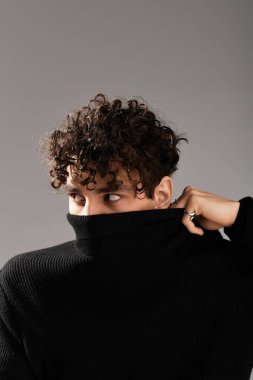 Kıvırcık saçlı genç bir adam cazibesini sergiler, modern uzayda şık bir aura oluşturur..