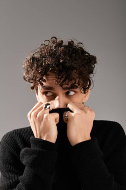 Şık bir genç adam, gösterişli kıyafetlerini ve aksesuarlarını gösterirken gülümsemesini gizler..