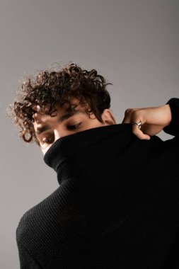 Kıvırcık saçlı yakışıklı genç adam siyah kazağını düzeltirken kendine güvenir..