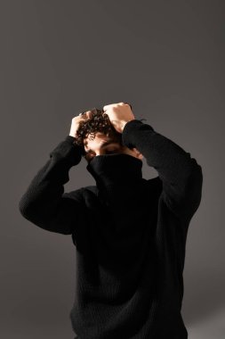 Kıvırcık saçlı yakışıklı genç adam, gri karşısında siyah giyinmiş cesur bir poz sergiliyor..