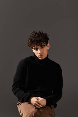 Kıvırcık saçlı çekici bir genç adam şık bir süveter giyer..