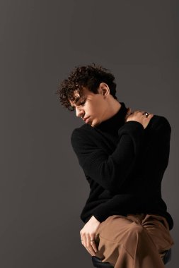 Genç adam minimalist bir stüdyoda kendine güvenini ve sanatsal yeteneğini yansıtan şık kıyafetler sergiliyor..