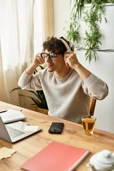 Rahat bir süveter giyen neşeli genç adam çalışma masasında çalışırken müzik dinliyor..