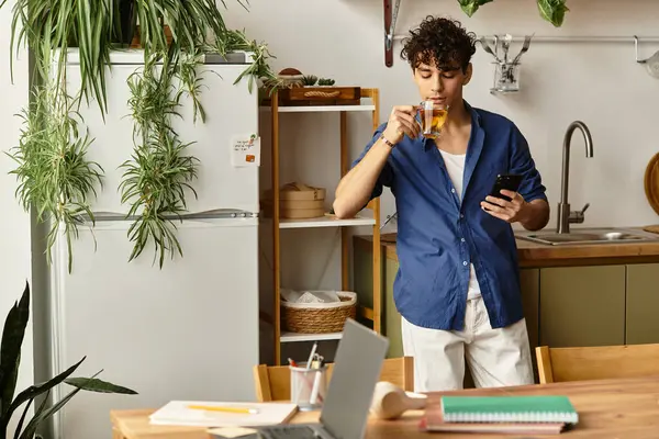 Şık bir genç adam, rahat ve telefonuyla bitkilerle dolu parlak bir mutfakta çayını yudumluyor..