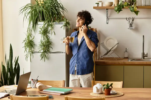 Şık genç adam telefonda konuşurken gülümsüyor, parlak bir mutfakta bir fincan çayın tadını çıkarıyor..