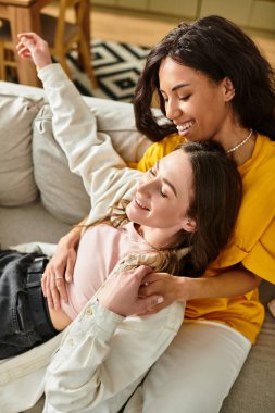 İki kadın, evlerinde birbirlerine eşlik ederken kucaklaşıp gülümseyen hassas bir anı paylaşıyor..