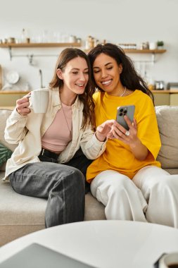 İki kadın sıcak bir gülüşü paylaşıyor. Oturma odalarında birlikte telefona bakıyorlar..